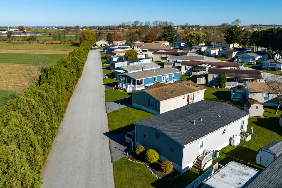 Aerial view of mobile home community in rural area with homes lined up diagonally next to small road.
